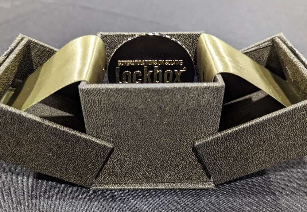 A gold challenge coin that reads "LOCKBOX" in an ornate box.