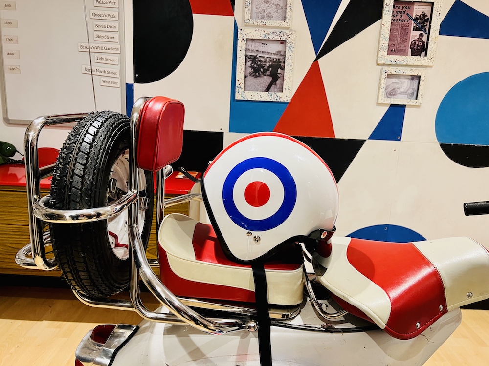 A colorful red, white, and blue motorcycle helmet with The Who logo, on a red and white motorcycle, in a red, white, blue, and black room.
