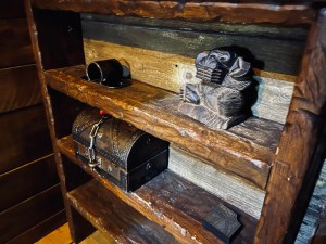 Old, imperfect wooden shelves with a monkey totem, a metal loop, and a small locked treasure chest.