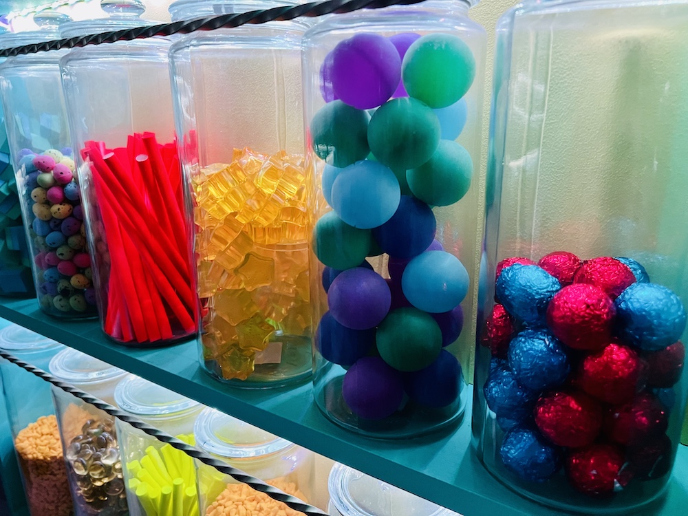 Closeup of tall glass jars on shelves, each filled with different candy.
