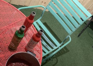 Brightly colored outdoor furniture in a fenced in backyard with empty beer bottles and a pot of beans sitting on the table.