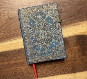A blue notebook with an ornate gold pattern. It has a metal clasp, and a red ribbon bookmark.