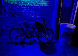 A bicycle with a backpack locked to a rack in a graphited alley.