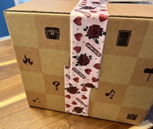A cardboard box with an assortment of illustrations on the side, sealed with custom packing tape that reads, "Suite Heart."