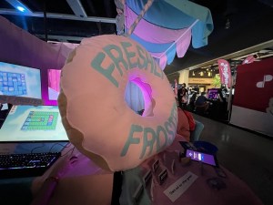 A giant yellow and blow donut display at a video game boot. The donut reads "FRESHLY FROSTED."
