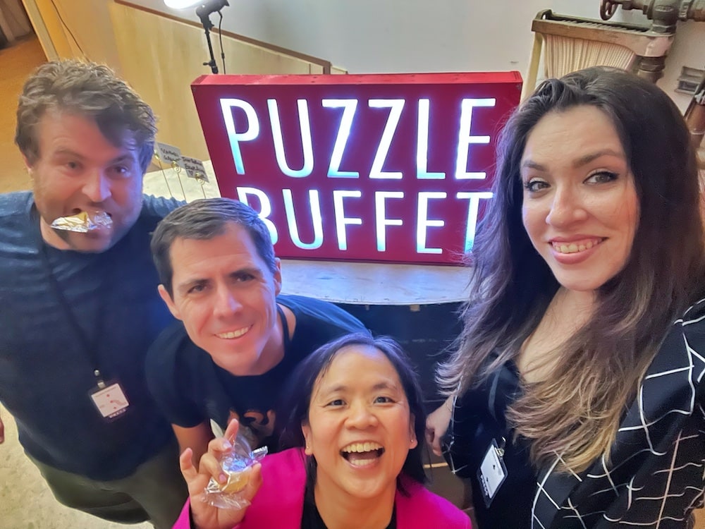 Cara, Tammy, Brendan, and Ryan holding up fortune cookies in front of an illuminated "Puzzle Buffet" sign.