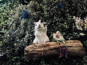 A little mouse sitting beside a fairy on a branch in a tree.