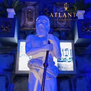 A statue of Poseidon in a temple. His spear is missing its trident. Text reads, "Atlantis the forgotten city"