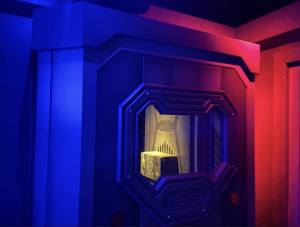 A metal compartment lit blue and red, inside is a metal box with a pattern carved into its face.