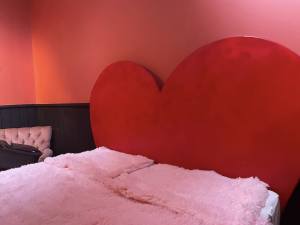A bed with a heart-shaped headboard covered in pink shag sheets.