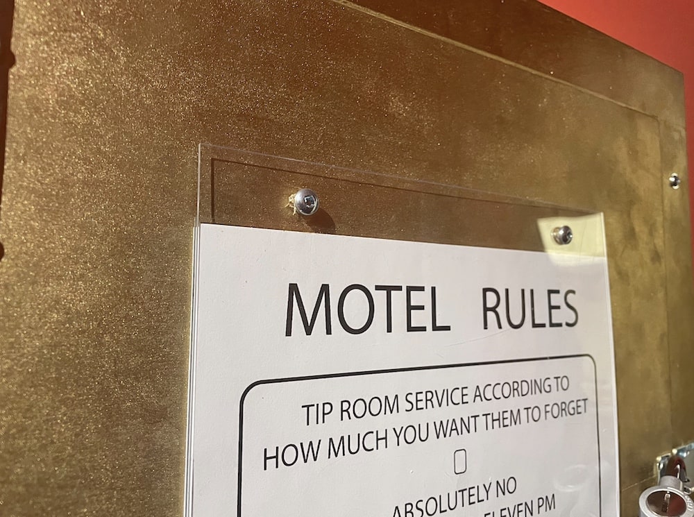A sign mounted in clear acrylic reads, "Motel Rules: tip room service according to how much you want them to forget."