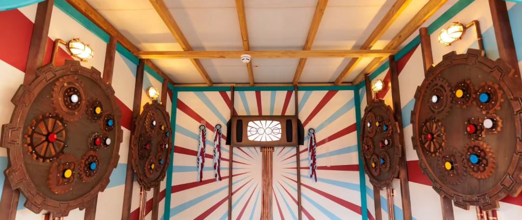 image of a room with colorful wallpaper. hung around are wooden frames containing various wooden gears. It seems to be a puzzle of some sort.