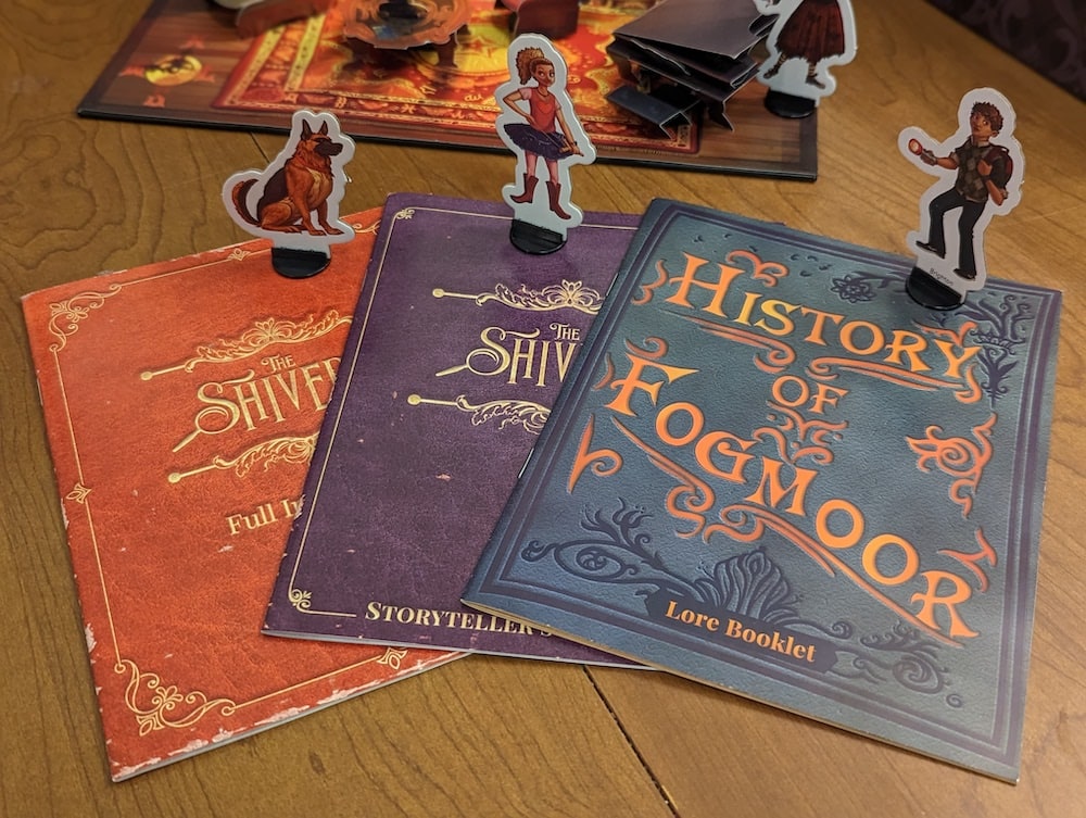 3 character stands atop 3 different booklets with lore, and instructions.