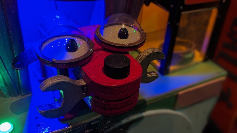 Closeup of a cute looking robot with big eyes and a wrench in its mouth.