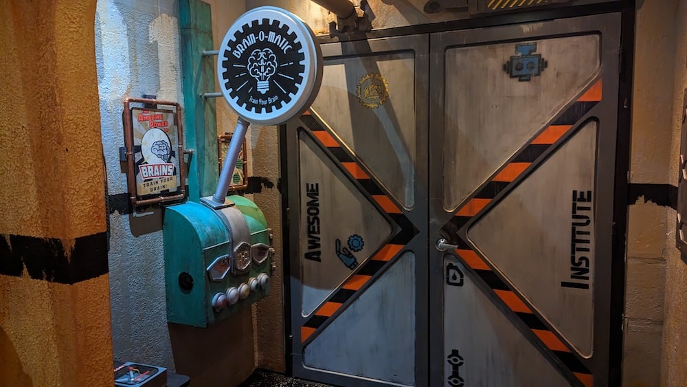 A strange device with a large sign that reads, "Brain-O-Matic." The device is mounted to the wall beside a large metal door with robot parts painted on it and the words, "Awesome Institute."