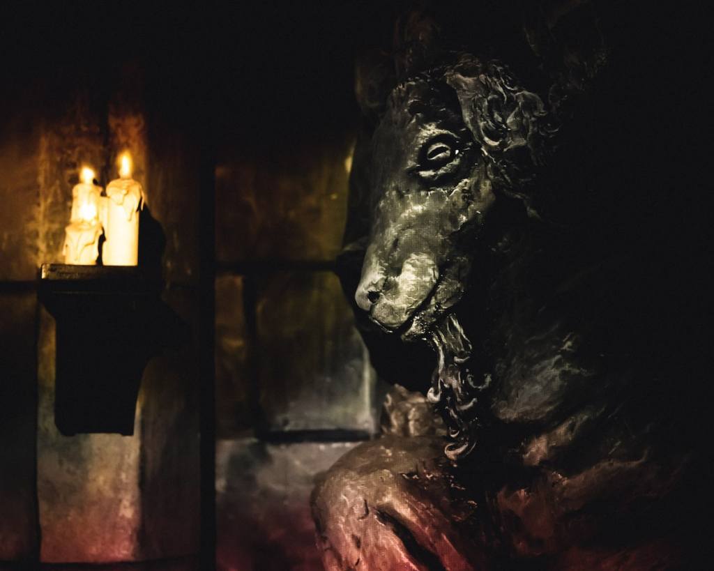 A stone goat's head mounted to the wall beside two lit candles.