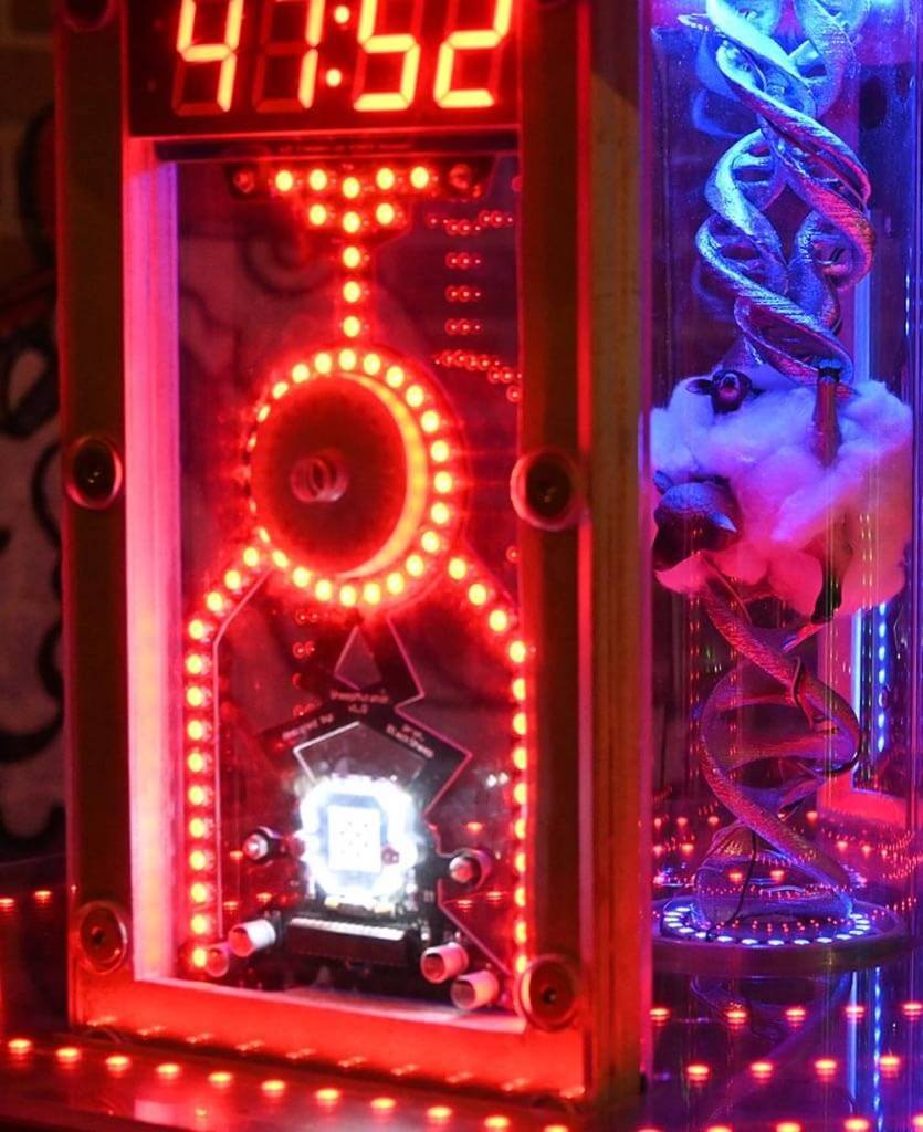 A strange machine with many red glowing lights and a sheep stuffed in a tube with DNA strands emanating from it.