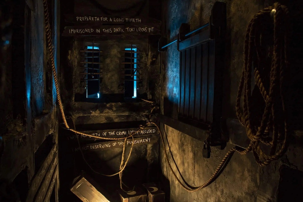 A dungeon corridor with a long strand of rope running through it, and words scrawled on wooden planks.