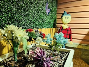 A scarecrow beside a flower box and a house.