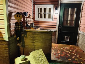 A scarecrow beside a leaf-covered, front porch.