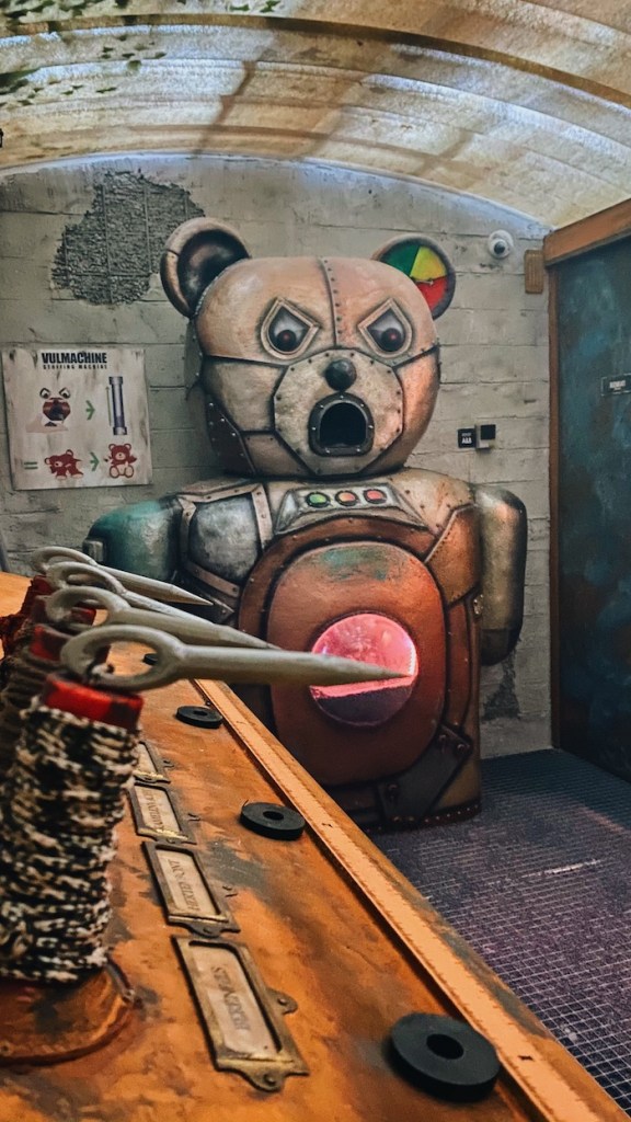 A massive mechanical teddy bear with a menacing face stands at the front of a control room.