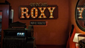 A large sign mounted to a wall reads, "The Movies Roxy" in lights.