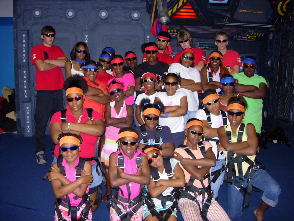 Approximately 24 elementary-aged students wearing sunglasses with their arms crossed.