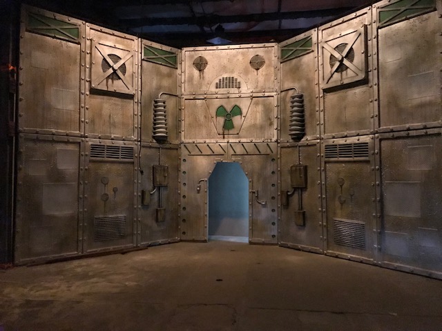 Imposing metal walls with a doorway under a large green radioactivity symbol.