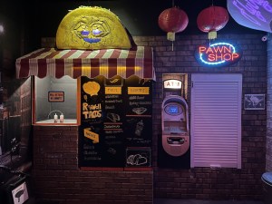 Roswell Tacos stand with an ominous oversized taco above the awning. Beside it is an ATM and a pawn shop.