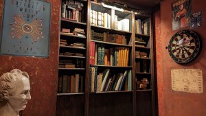 A study with bookshelves filled with books, and a dartboard hung on the wall.
