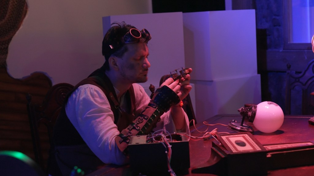 an with steampunk googles on his forehead and smudges of dirt on his cheek thoughtfully examining a gadget.