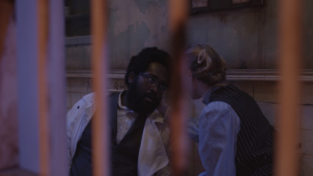 looking through bars at two characters sharing a scene