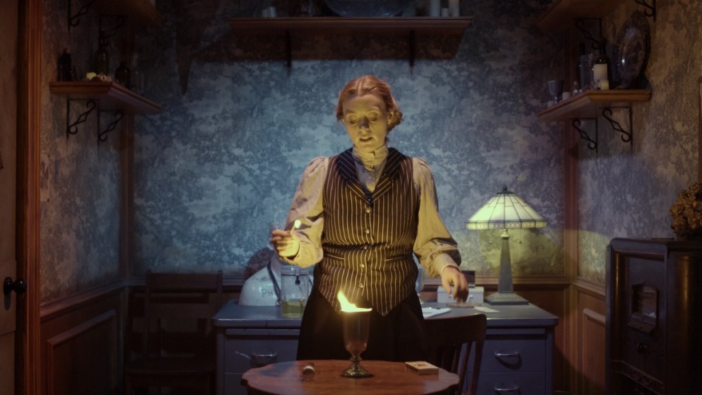 a woman in a study, standing in front of a table where a goblet sits aflame