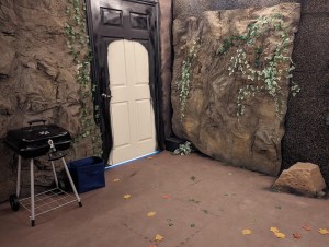A cave with a typical house door. A barbecue grill is locked in the middle of the room.