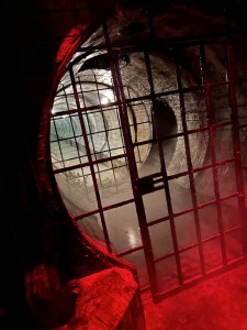 A metal gate in a dramatically lit sewer tunnel.