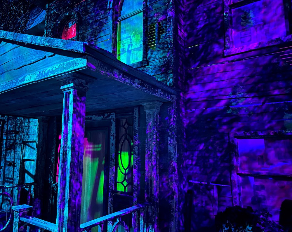 Exterior of an old, rundown home. It is imposingly lit in purple and green.
