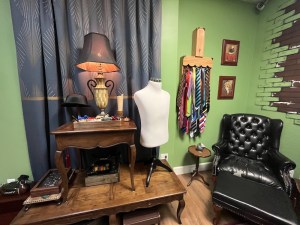 A tailor's workspace with hats, neckties, sewing equipment, and a large black leather chair.