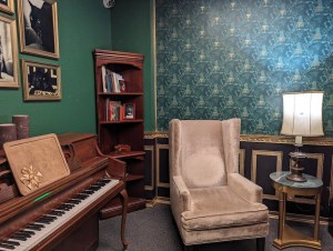 An elegant living room with a large chair, a piano, and many framed photos of a black cat.