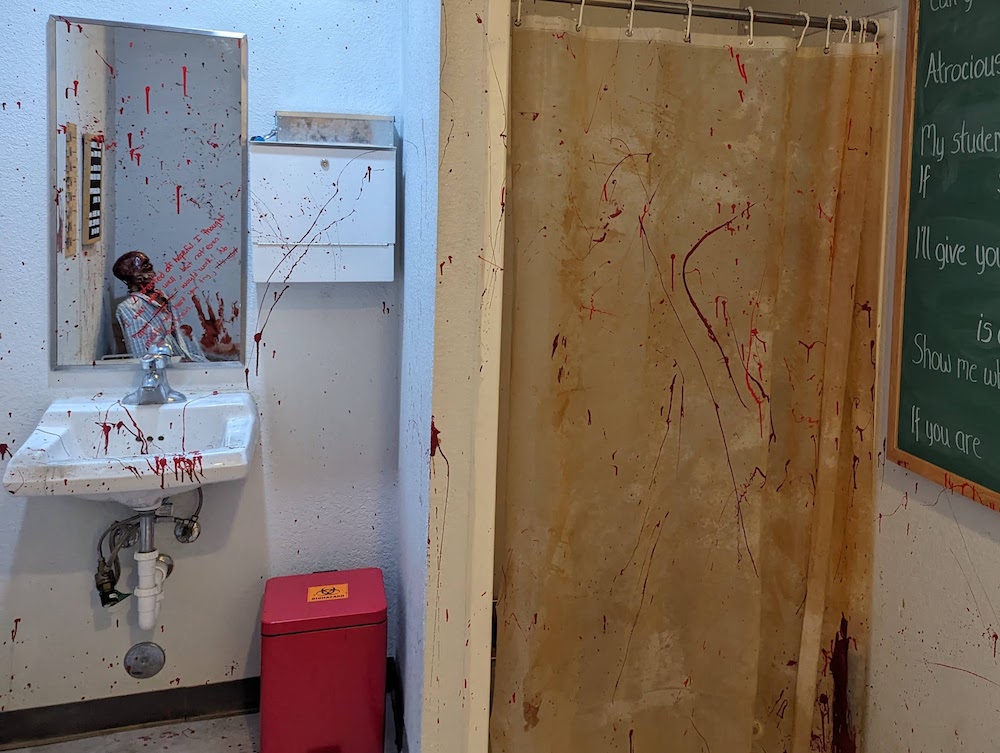 A bathroom sink, mirror, and shower curtain in a medical lab. Everything is covered in blood spatter.