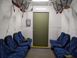 The back of a transport with seating on either side. supplies hang in cargo nets above.