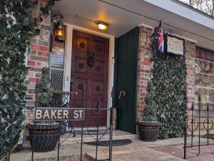 Exterior front door of the Sherlock Hom with a British flag and a "Baker St" sign.