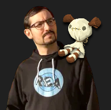 man with glasses in a black hoodie. there is a voodoo doll on his shoulder