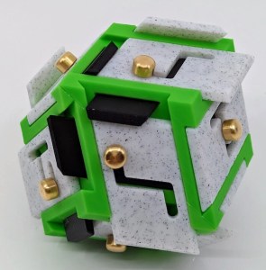 An unuqual puzzle made from greet, gray, and black pieces, with sliding brass pins in channels.