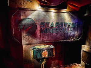 A dramatically lit, large, rusting metal sign for "Starstrike Minerals"