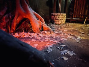 The floor of a forest in autumn. A brick well is off in the distance.