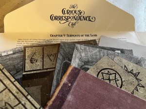 Closeup of an assortment of items from the Curious Correspondence Club along with a note introducing Chapter 5.