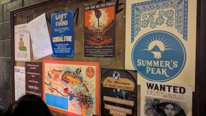 A billboard filled with posters for things happening at Phantom Peak during Summer's Peak.