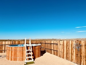 An above ground pool in a fenced-in area in the middle of the desert.