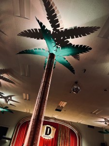 An ornamental palm tree, dramatically lit with the Club Dosselmeyer stage beyond it.