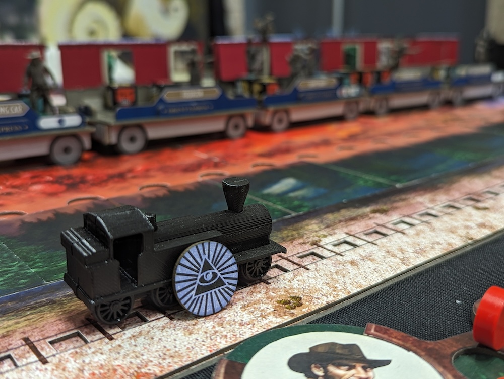 Closeup of a train game piece with a RECON-like triangle and eye token leaning against it.